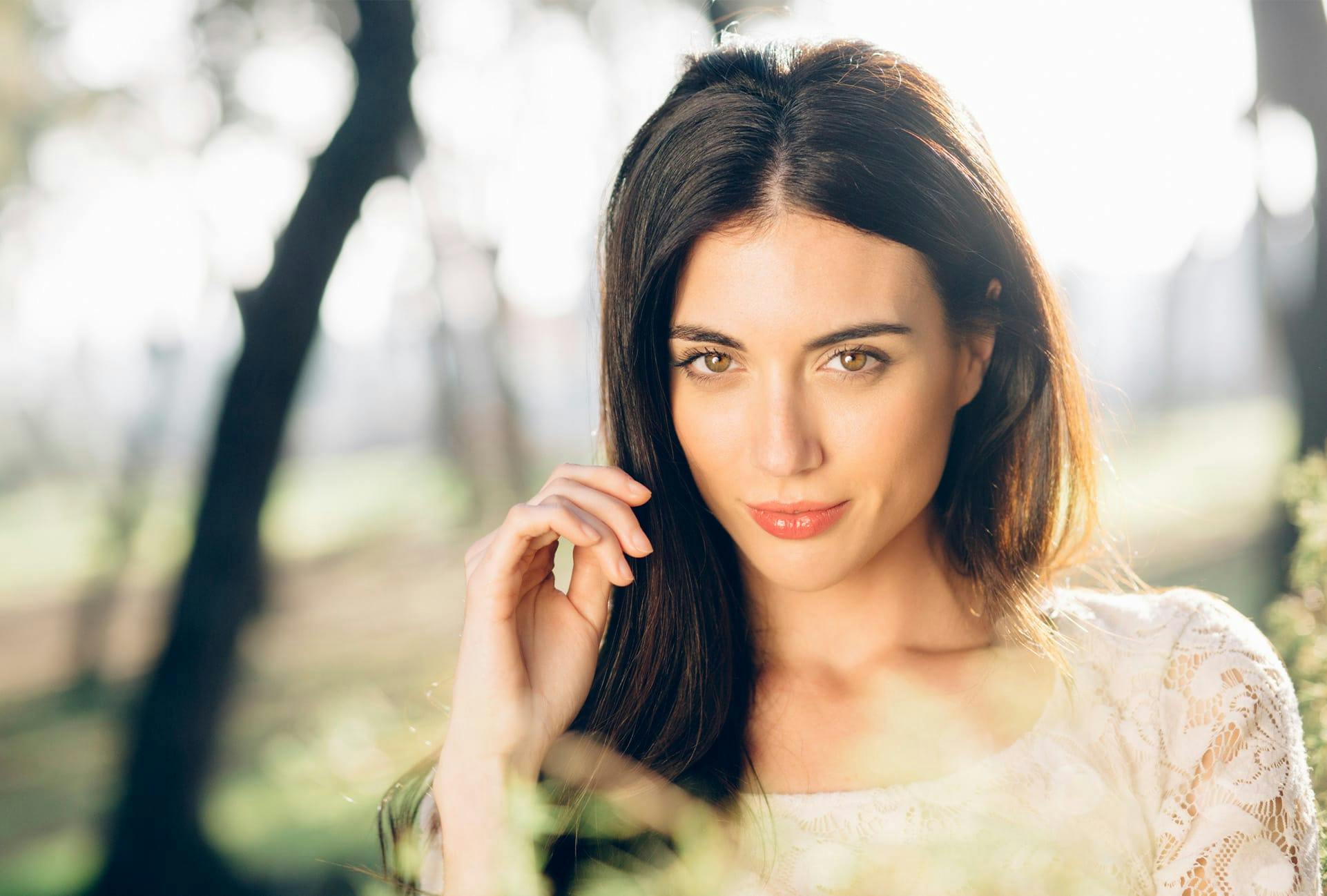 Woman next to some trees with her hand near her face