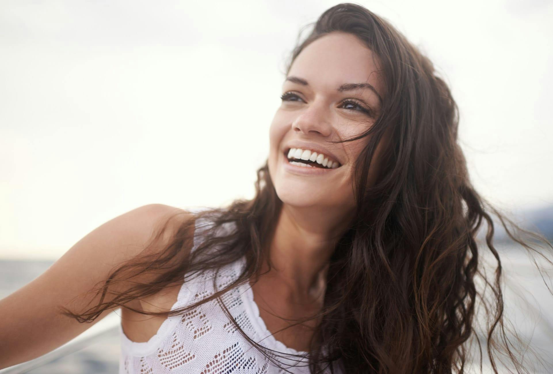 Woman with wavy dark hair smiling on the beach