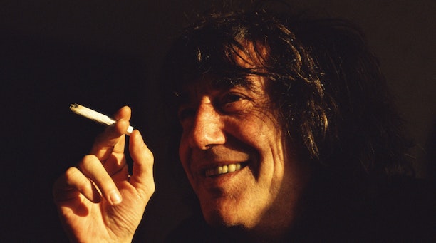 A smiling man holds a cigarette