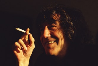 A smiling man holds a cigarette