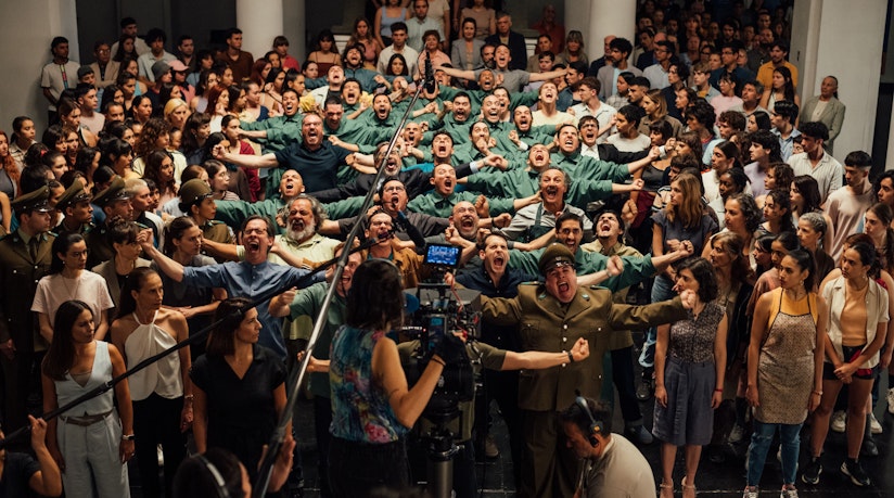 A large group of people can be seen opening their mouths and spreading their arms on a film set