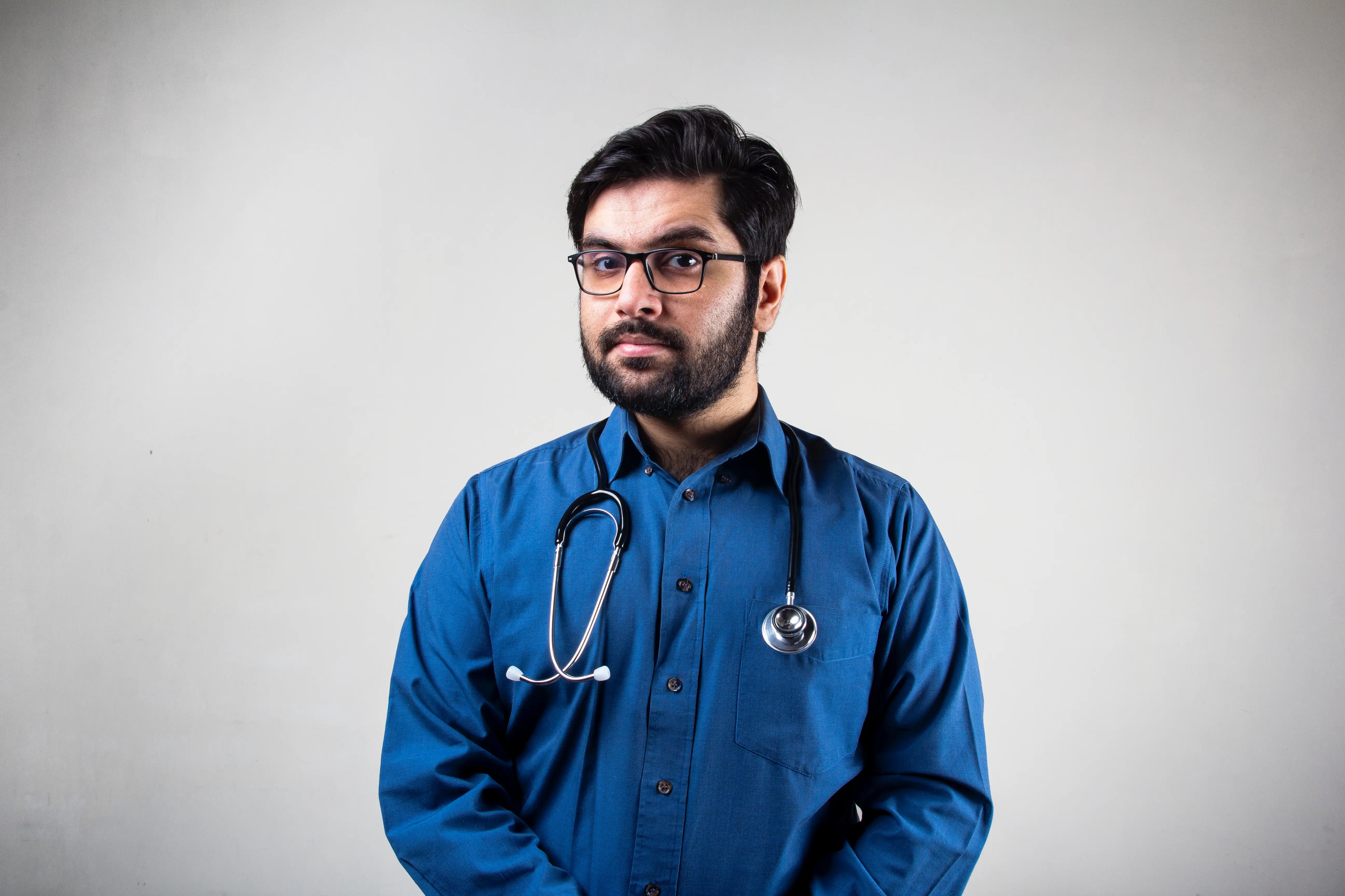 A doctor with a blue gown and a stetoscope looking at the camera