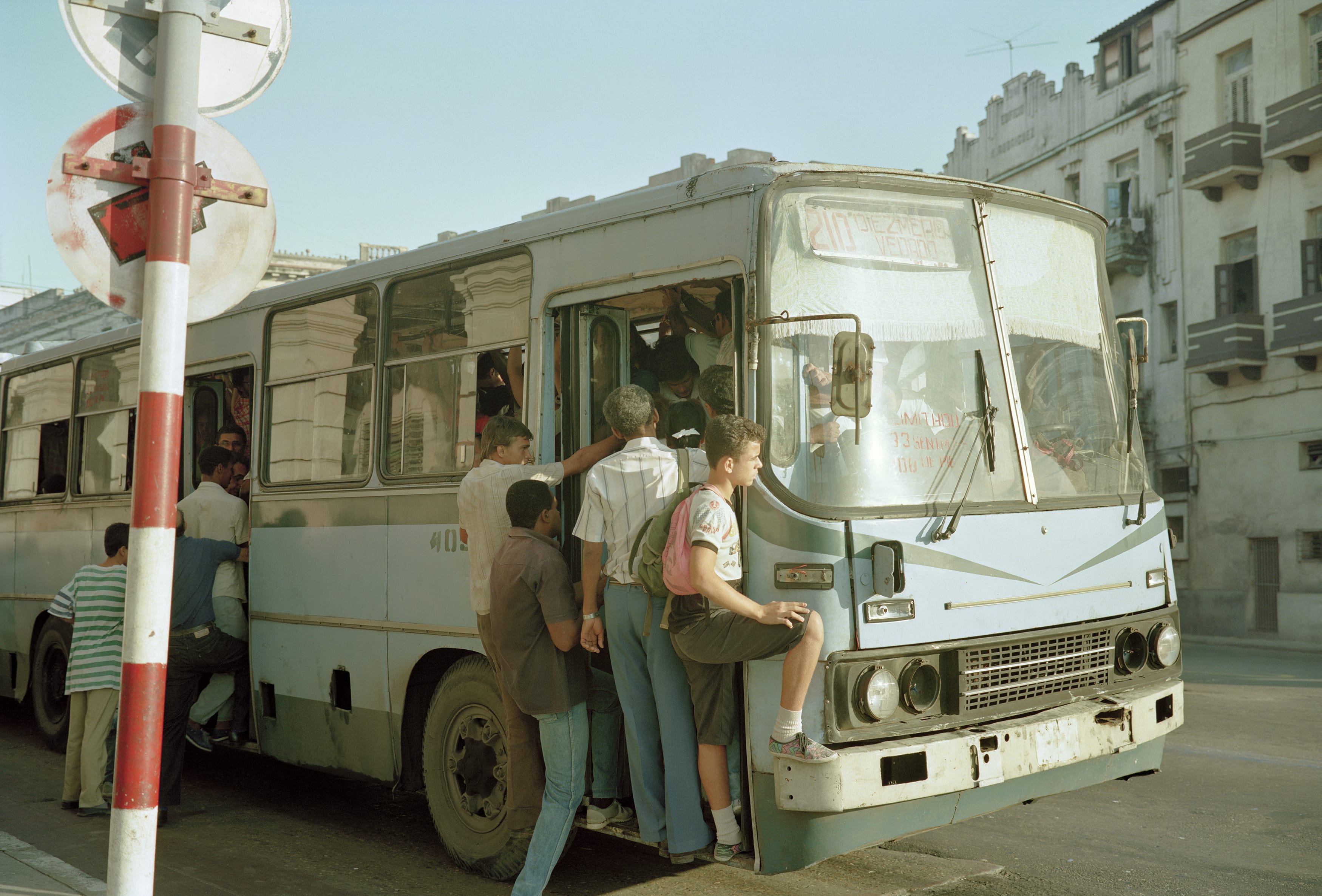 An overcrowded public bus (guaguas, as they are called in Cuba) rides through Central Havana. During the 1990s “Special Period,” fuel was scarce, and transportation was difficult. Over-flowing buses were a common sight during this time.