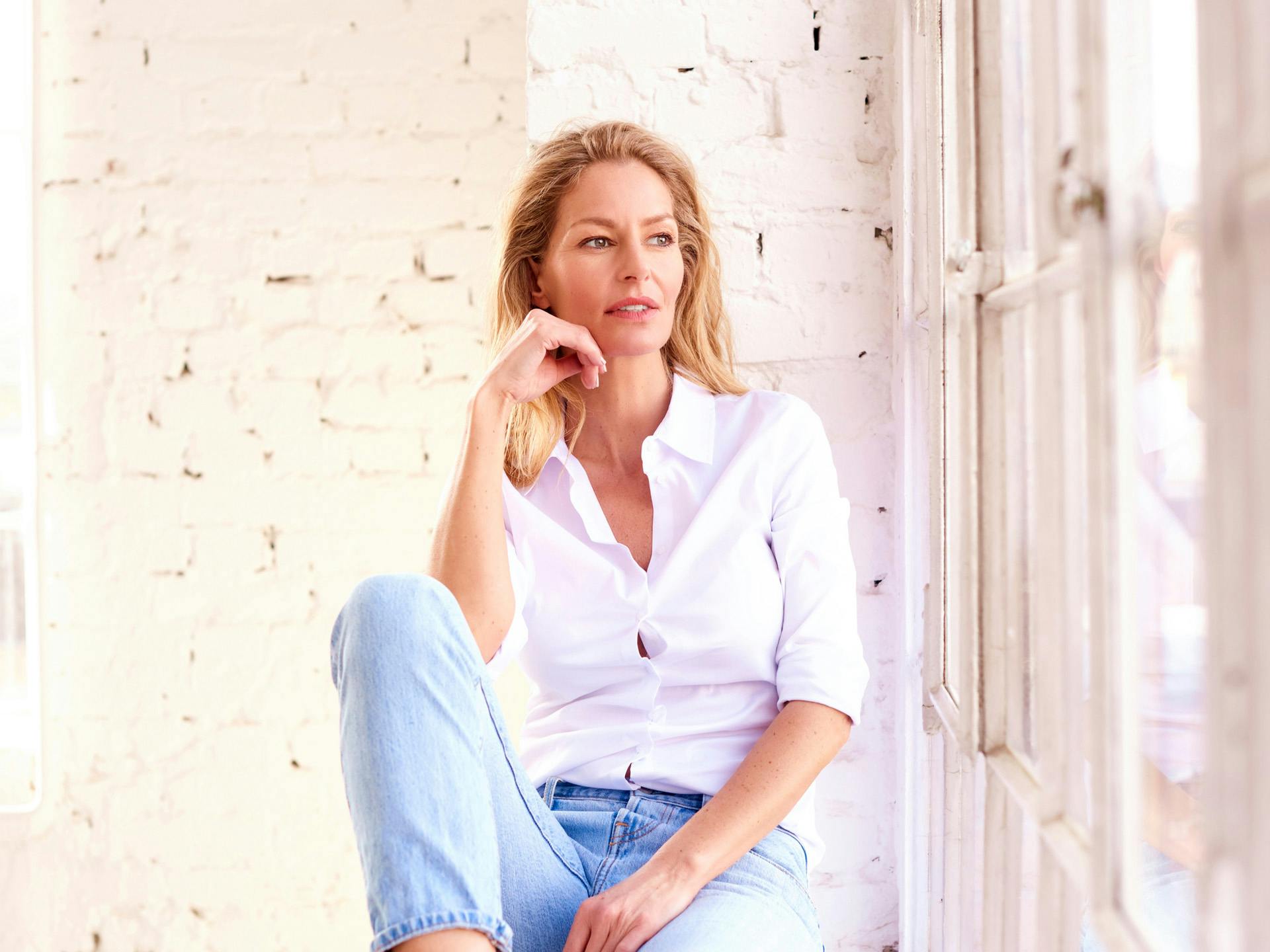 Woman in white button down resting her face on her hand