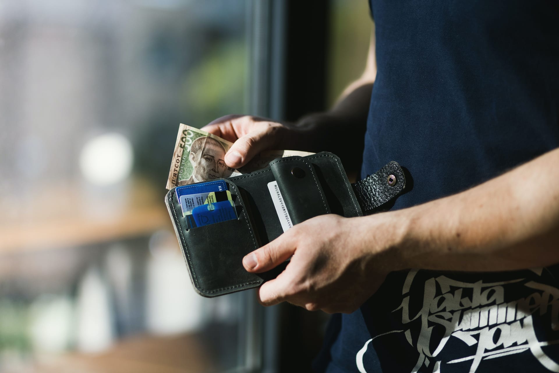 Man’s hands holding a black wallet with money and credit cards