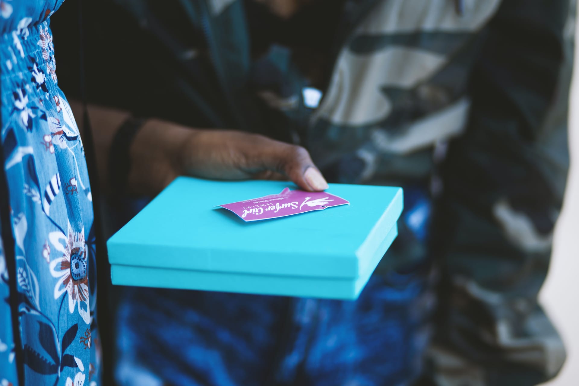 A hand holding a blue, square gift alongside a purple card