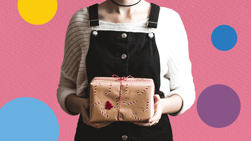 Woman holding decoratively wrapped gift package against a pink background.