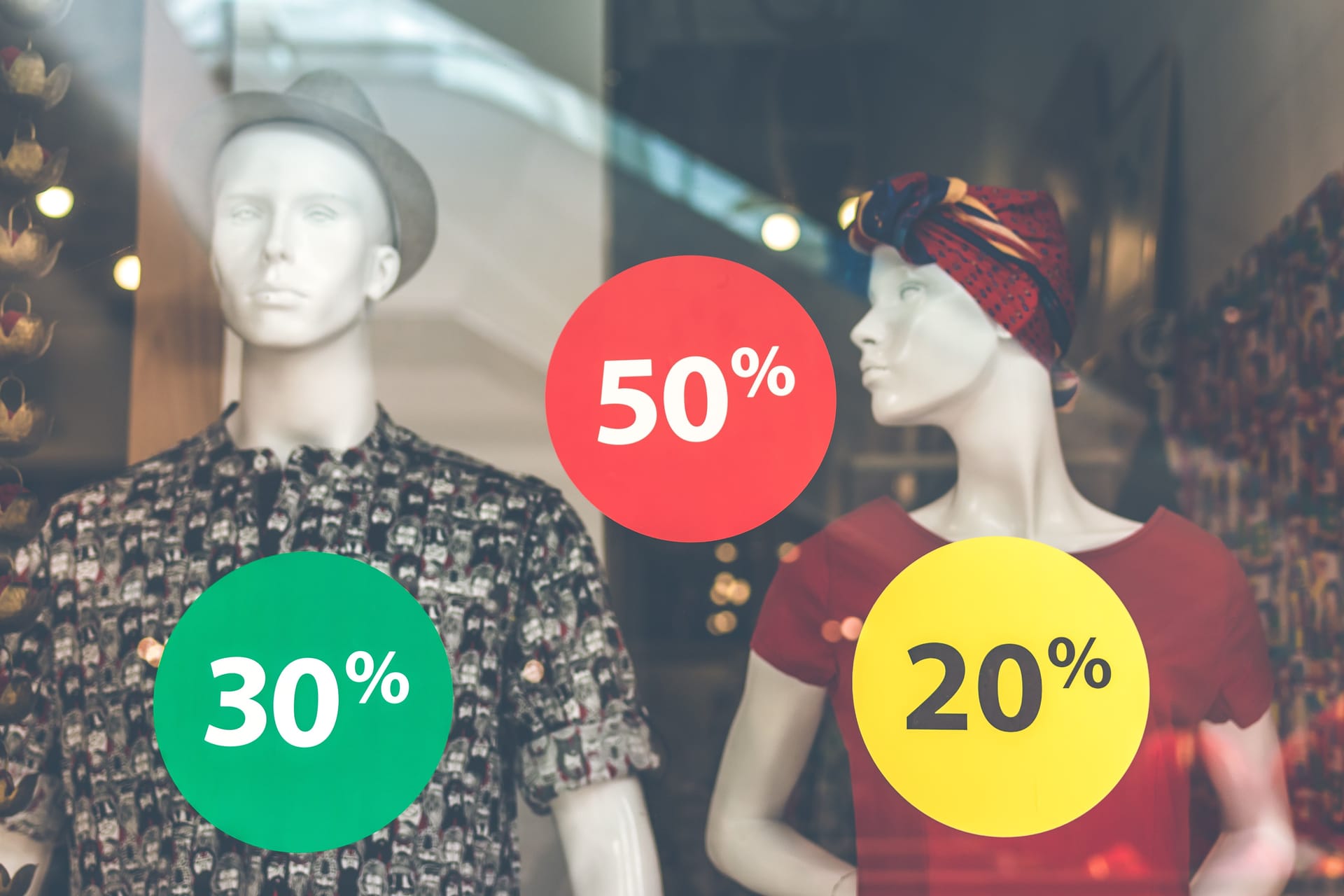 Mannequinin a store window display with huge savings advertised.
