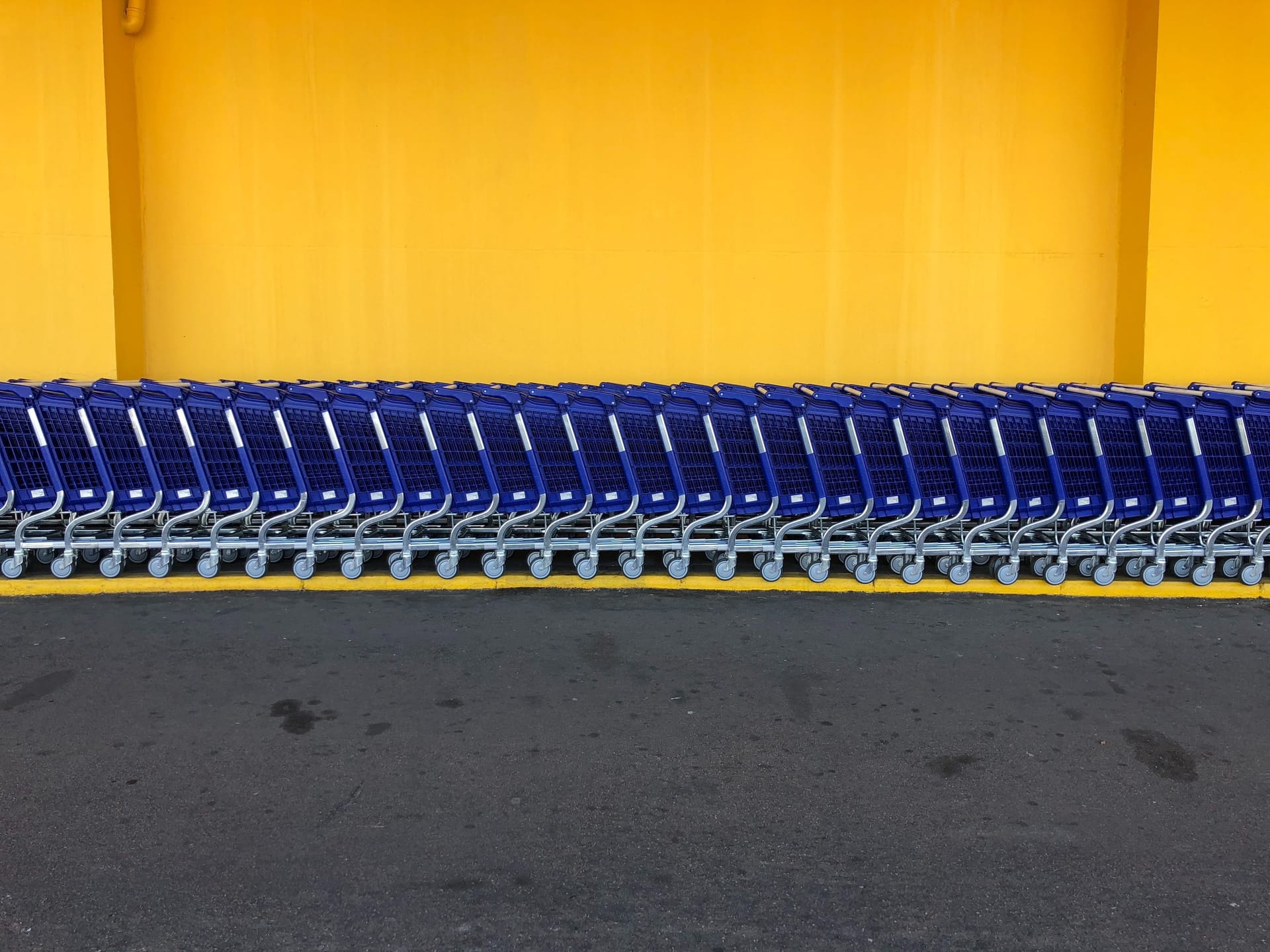 A line of blue Walmart shopping cards lined against a yellow wall.