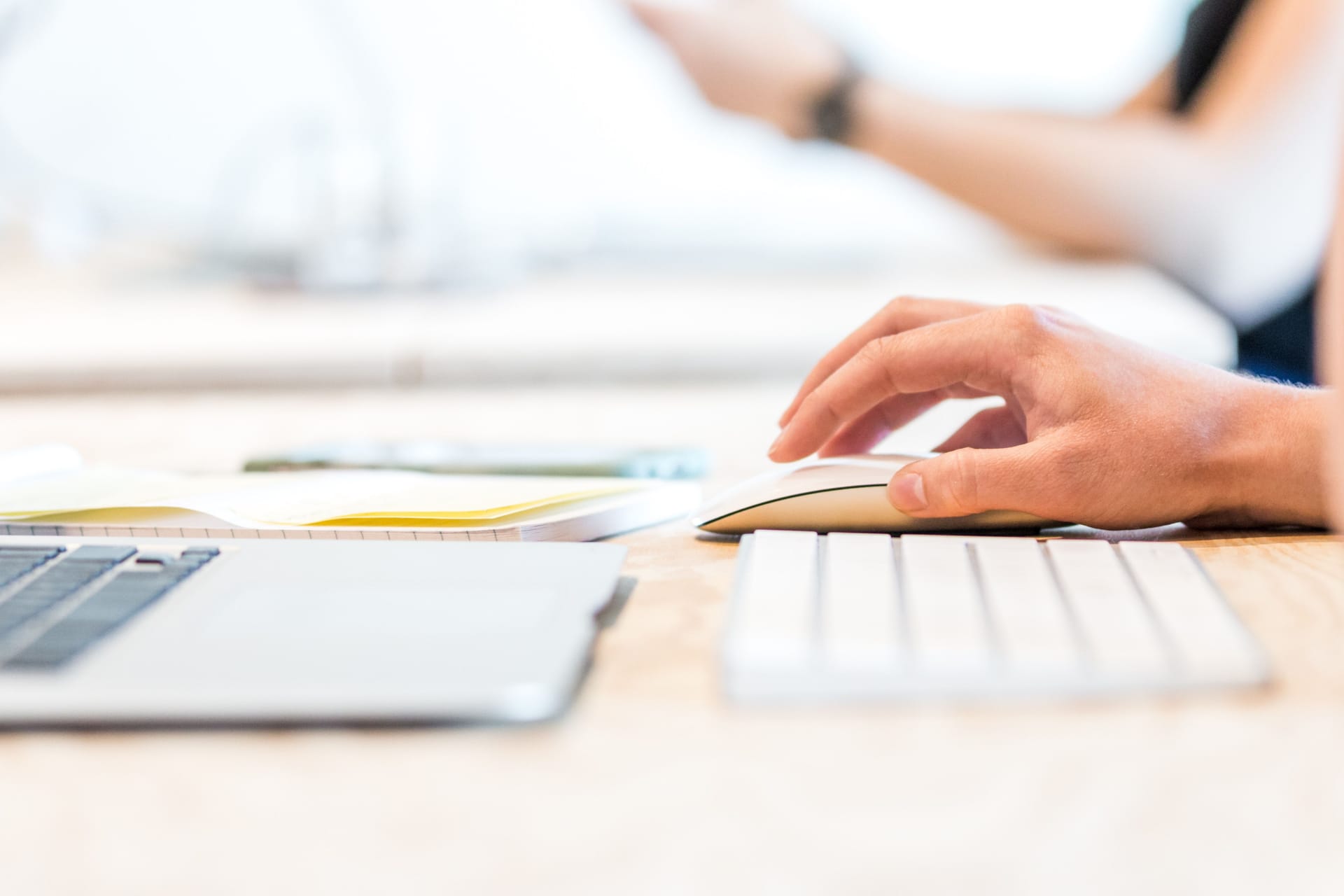 A hand holds a mouse next to a laptop and keyword.