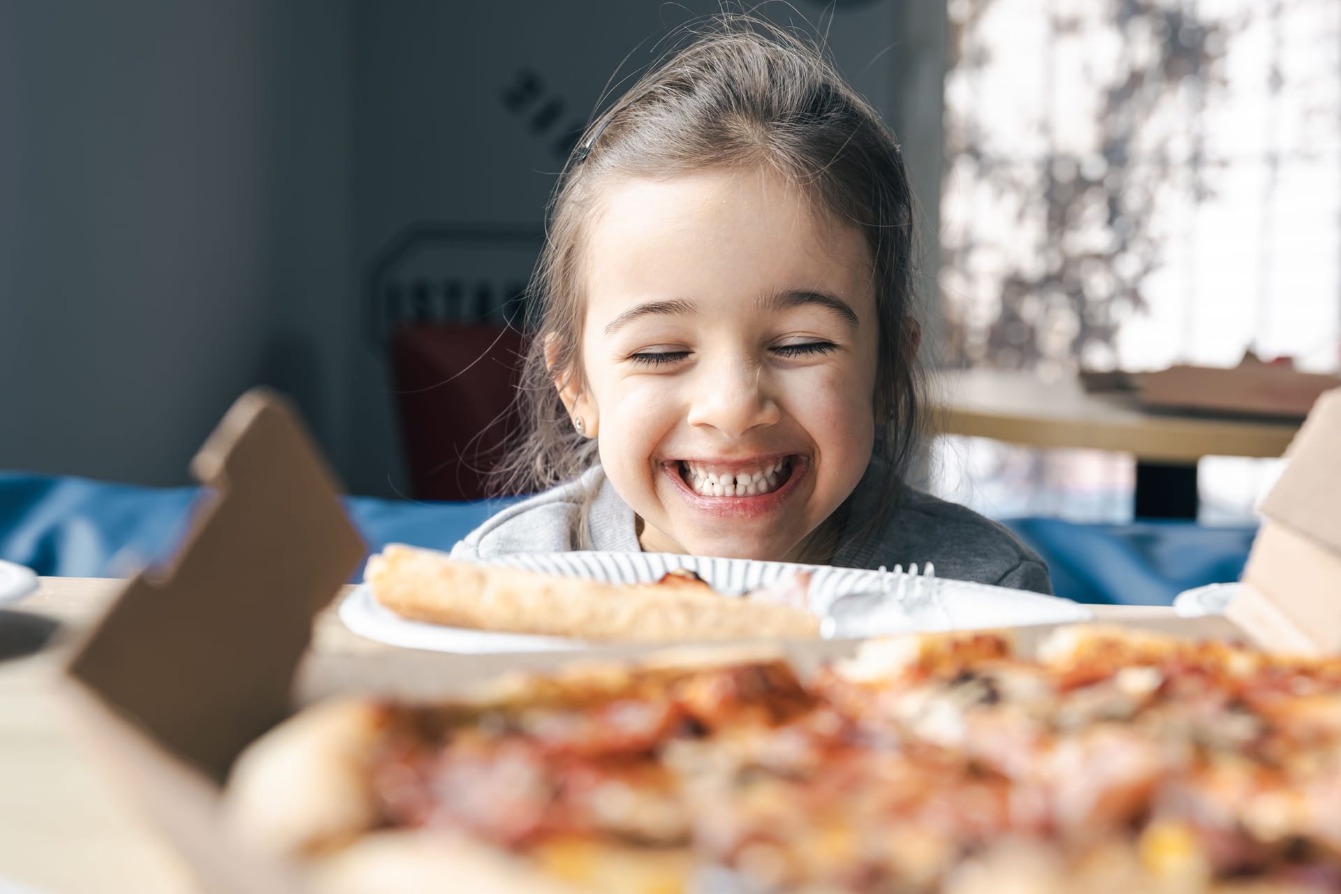 Happy little girl looking at a pizza with appetite.