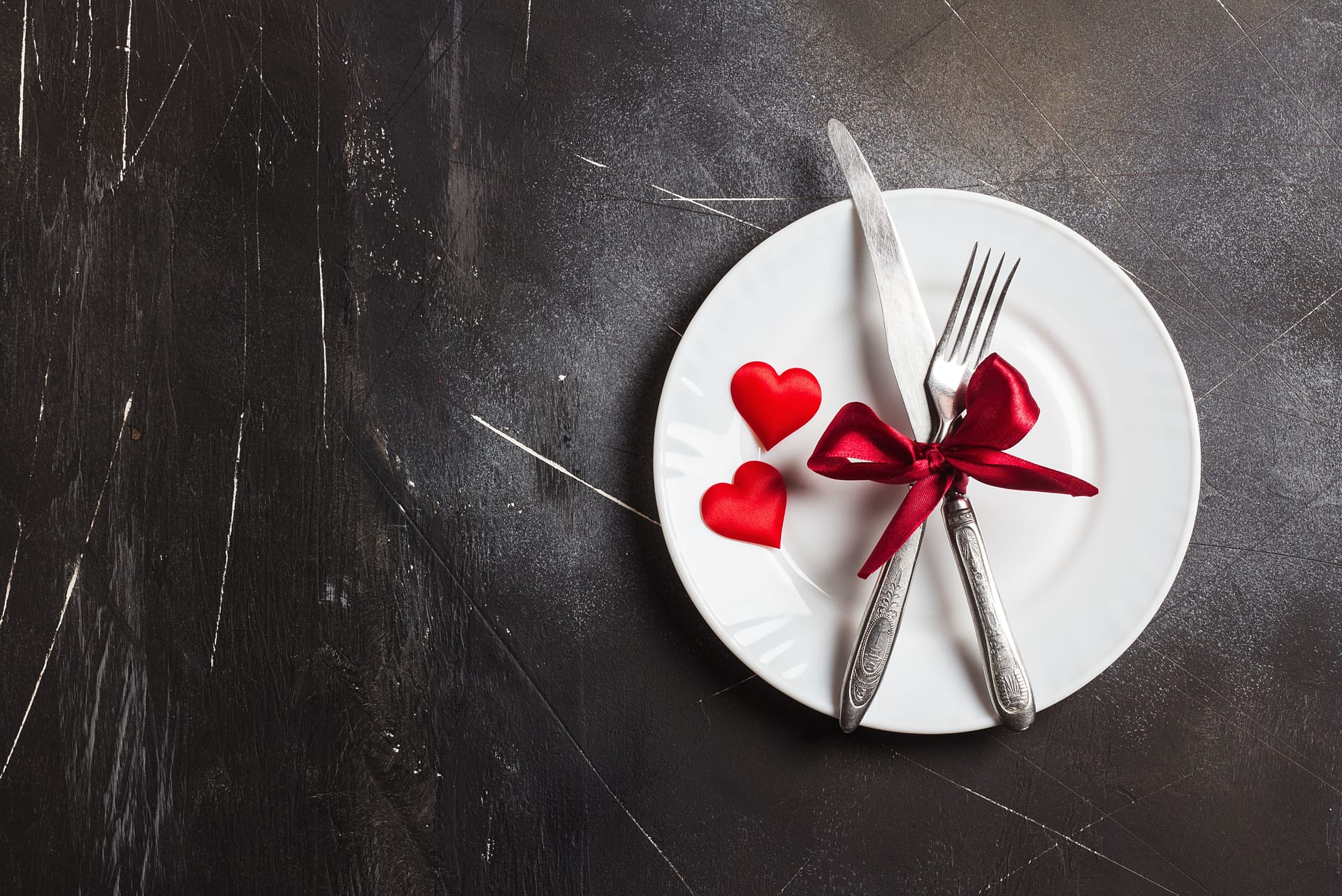 Ribboned cutlery and 2 red hearts on a white plate.