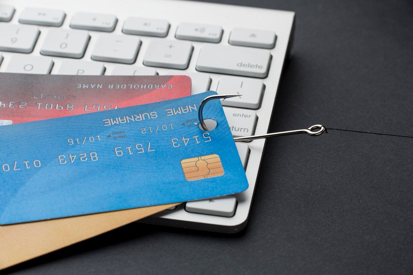 3 different colored credit cards on a keyboard are being hooked away by a fishing hook.