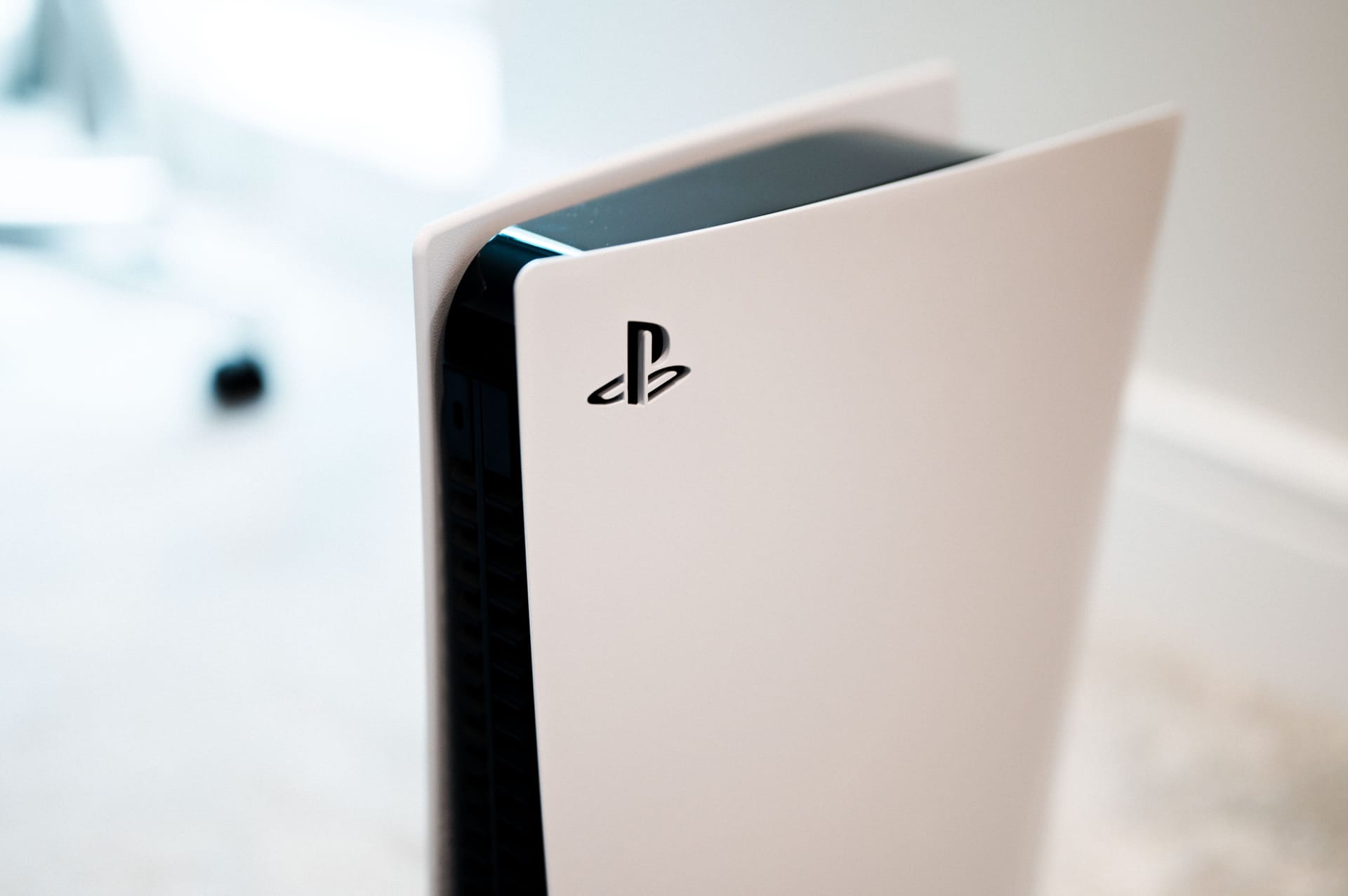 Bild einer senkrecht stehenden PS5 vor einem verschwommenen Hintergrund, der Bildfokus liegt auf dem PlayStation-Logo.