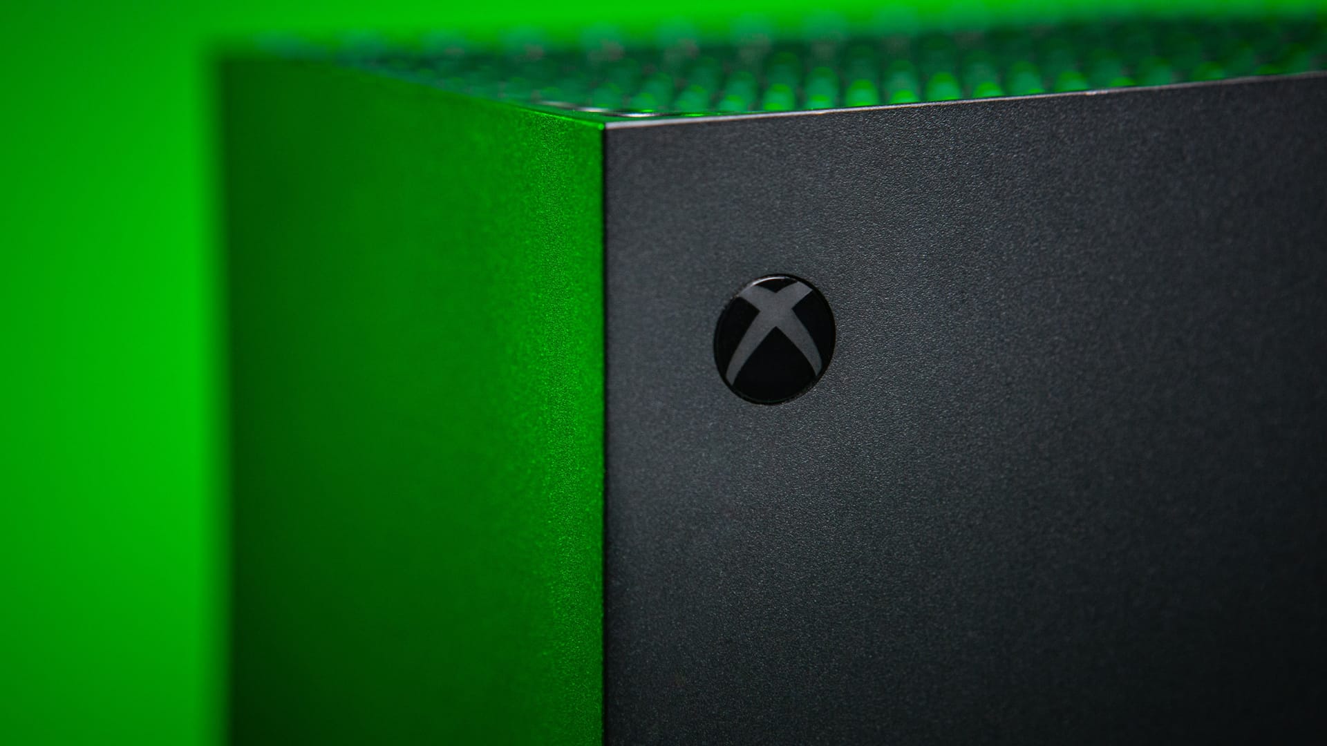 Ein Bild der oberen Ecke einer Xbox Series X vor hellgrünem Hintergrund. Der Bildfokus liegt auf dem Konsolen-Logo.