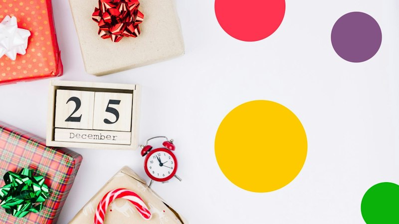 Geschenke auf einem weißen Tisch, umgeben von einem Wecker und einem Kalender, der das Datum des 25. Dezembers anzeigt.