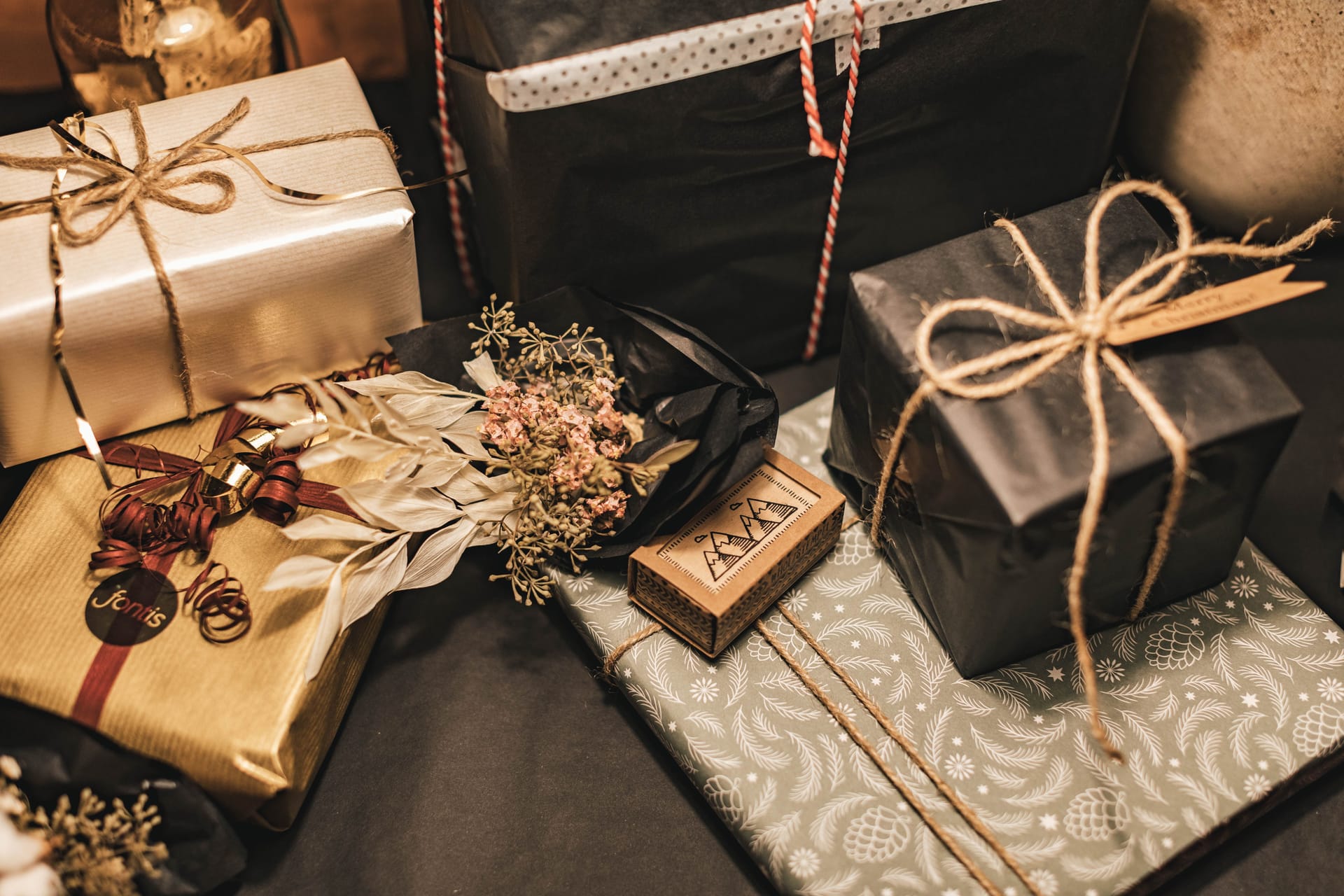 Ein Stapel Weihnachtsgeschenke auf einem dunklen Untergrund, die in schwarz-goldenes Geschenkpapier verpackt wurden.