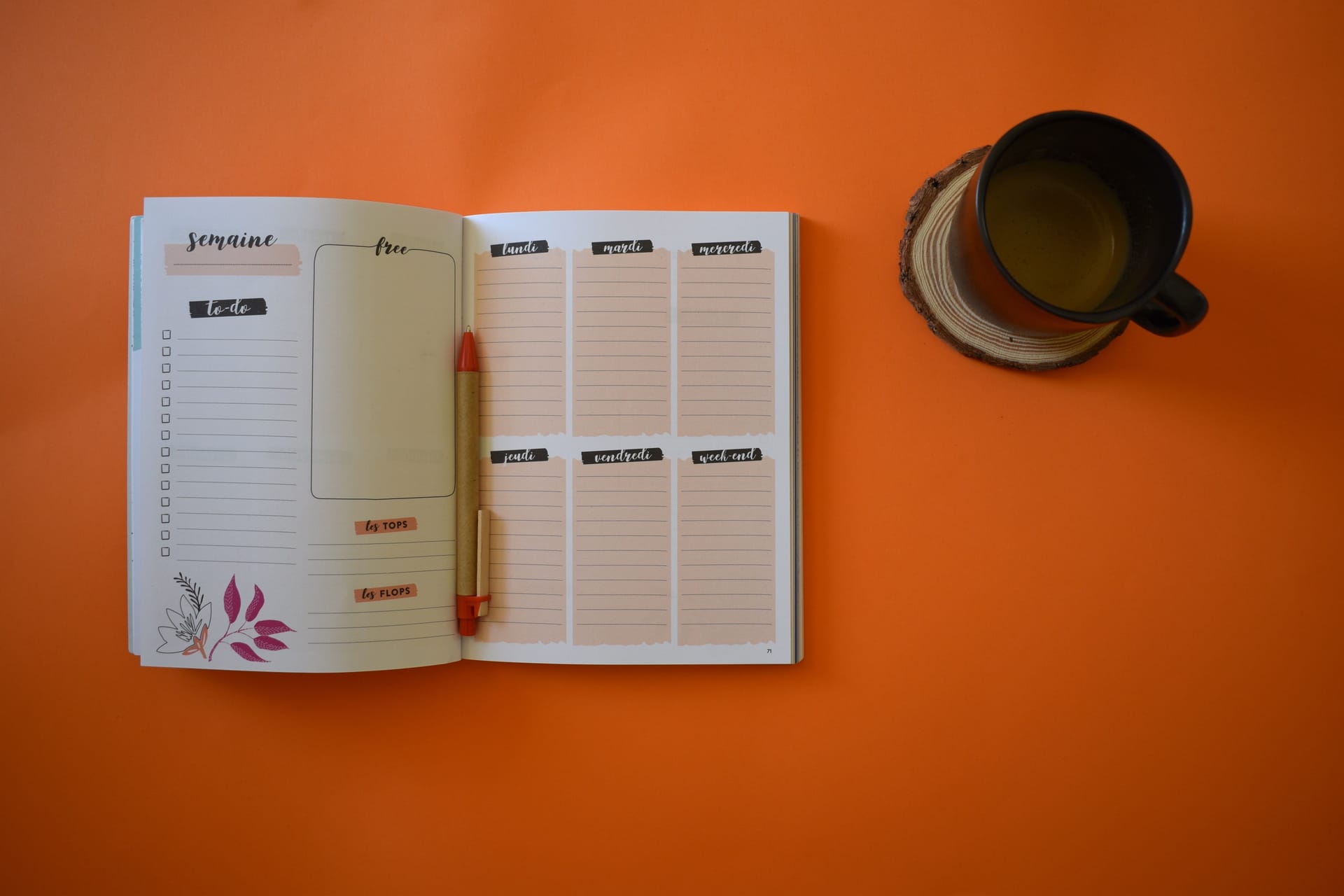 A weekly agenda with a pen on an orange background, alongside a cup of coffee in the corner
