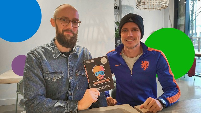 L'auteur Koen Schobbers et un intervieweur de Bundle assis à une table, tenant le livre "My Gambling Child", entouré de sphères de différentes couleurs.