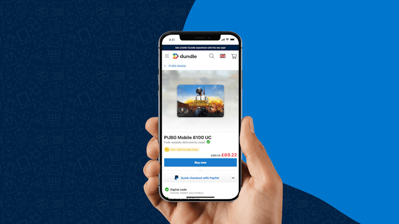 A hand holding a smartphone with the dundle webpage open on the PUBG Mobile 8100 UC product page showing the price of £69.22 and “Buy now” button.