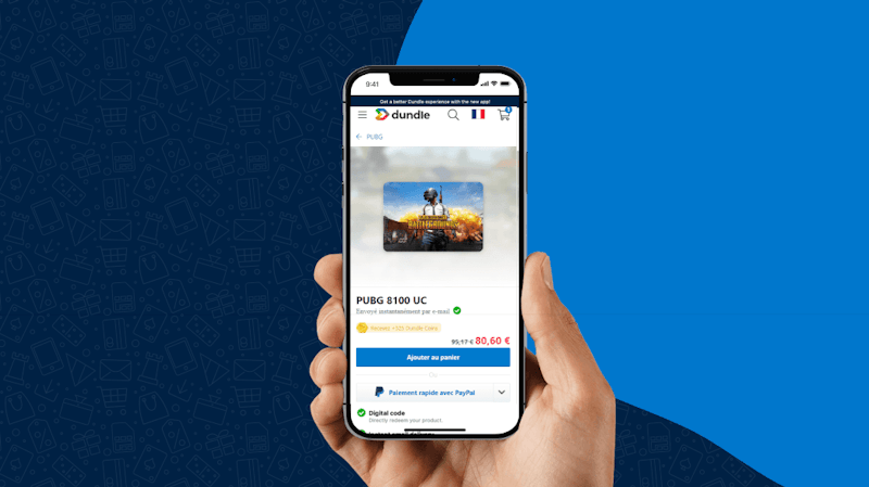 Une main tenant un smartphone ouvert sur la page du site dundle pour acheter 8100 UC PUBG Mobile pas cher au prix de 80,60 € (au lieu de 95,17 €) et le bouton "Ajouter au panier".