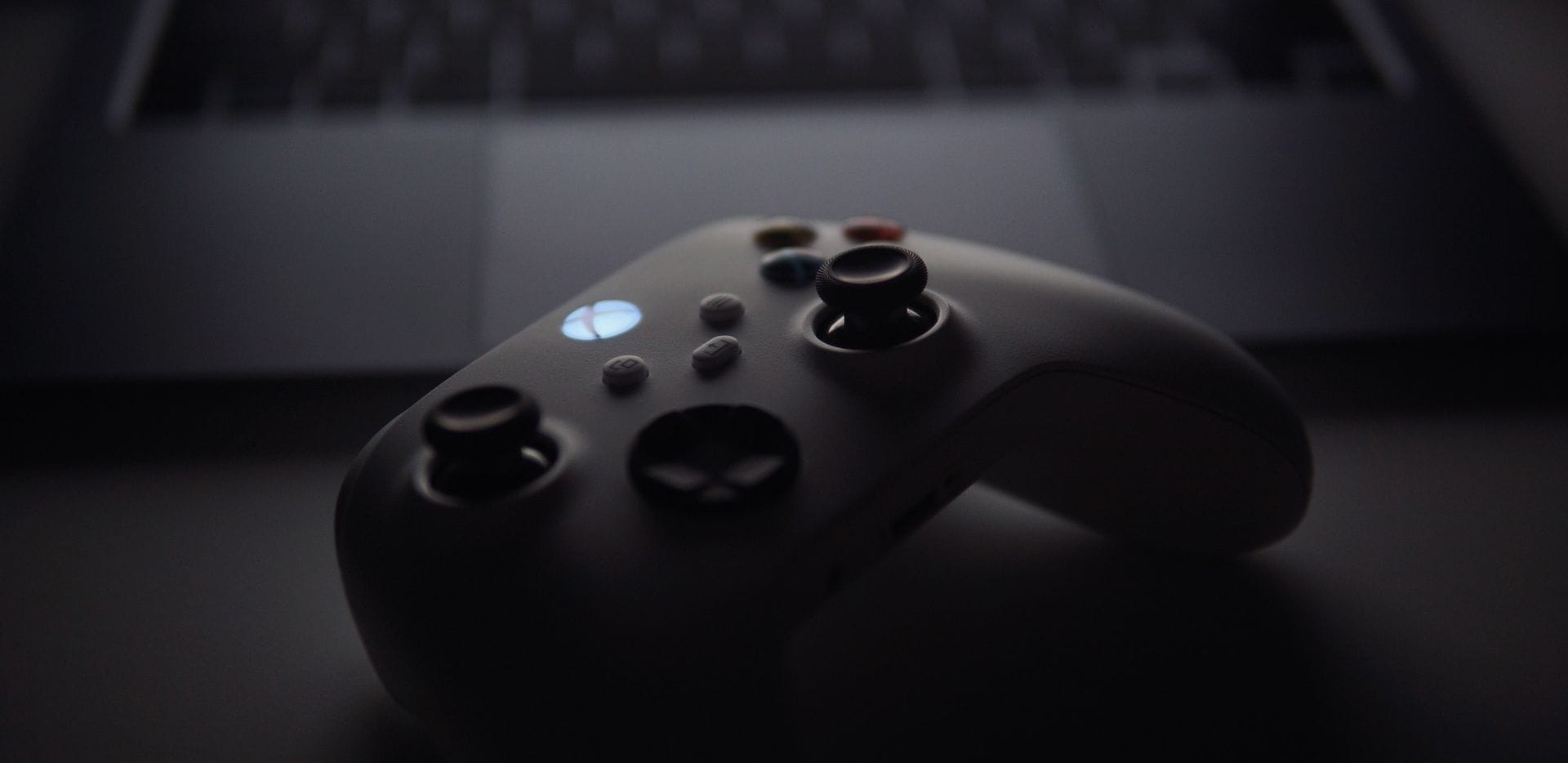 Dark picture of an Xbox controller in front of a laptop.