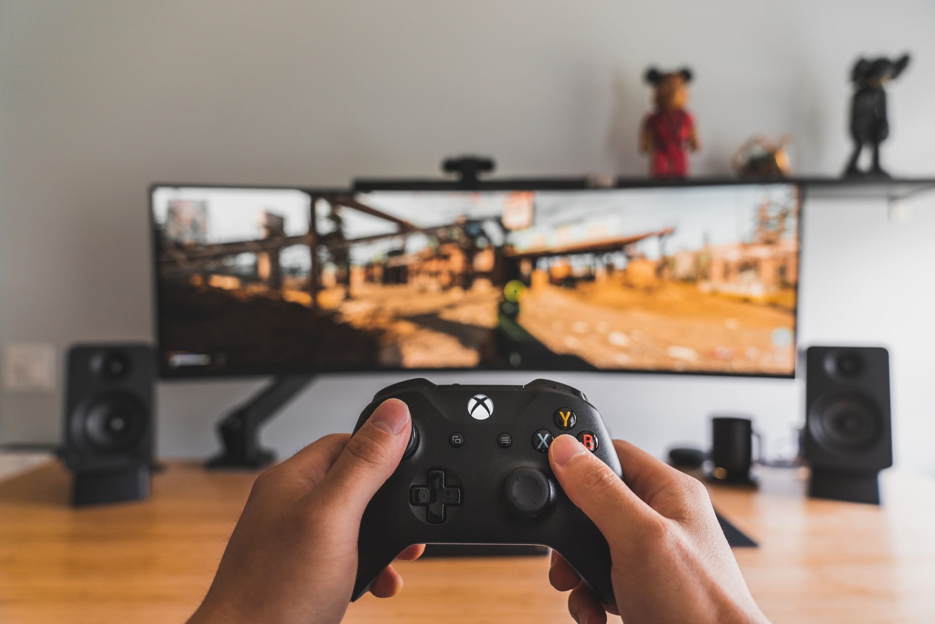 Two hands holding a Xbox controller in front of a big computer screen playing a game.