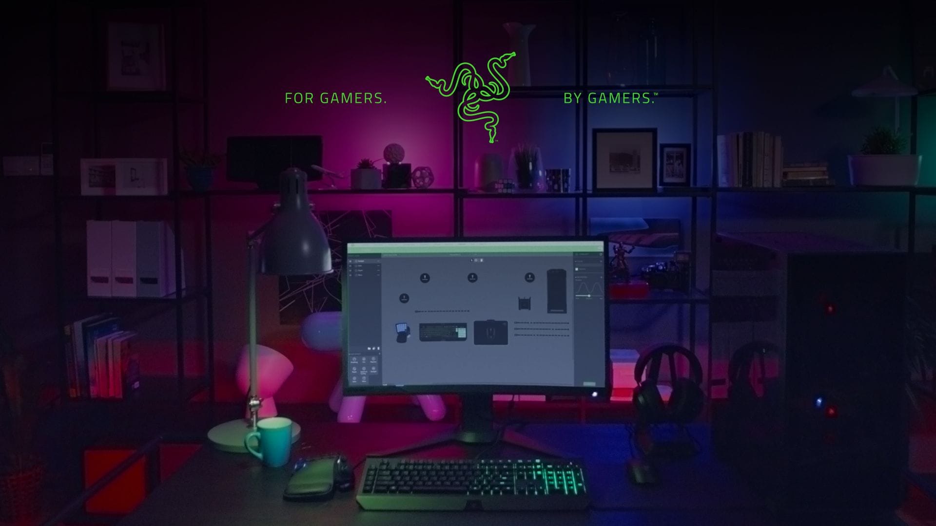 Ekran monitora na tle pokoju biurowego. U góry znajduje się zielone logo Razer z napisem “For Gamer by Gamers”.
