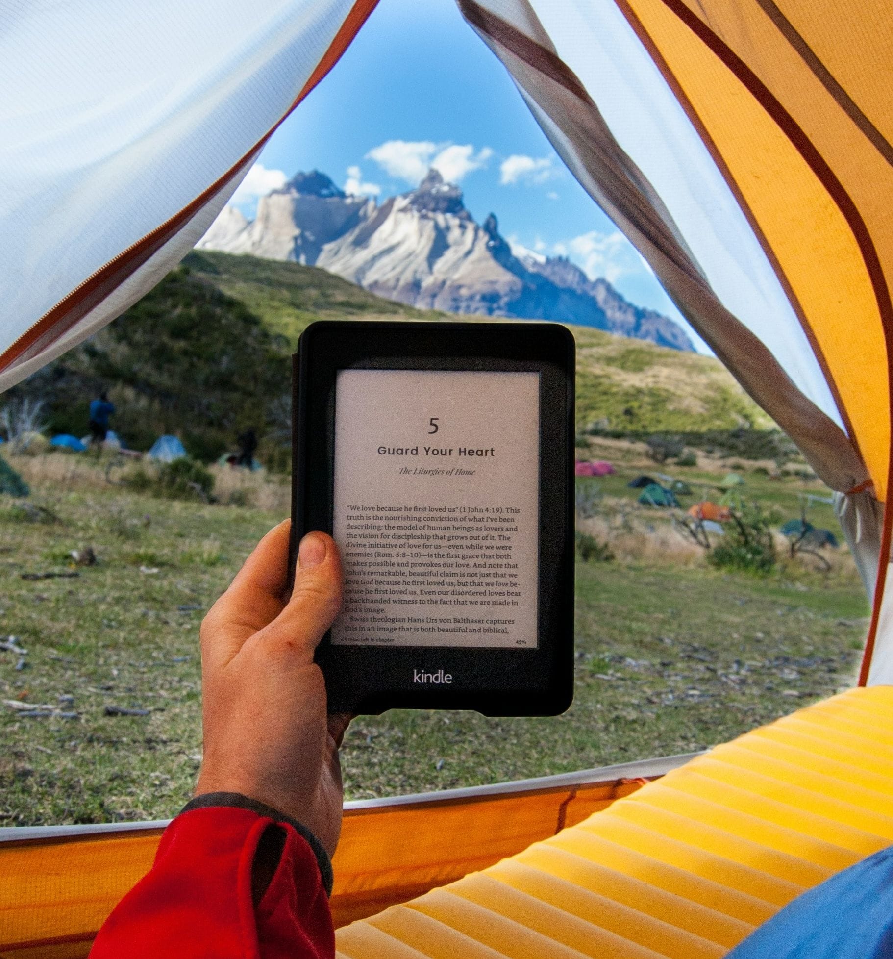 Iemand leest een ebook terwijl diegene kampeert op een berghelling.