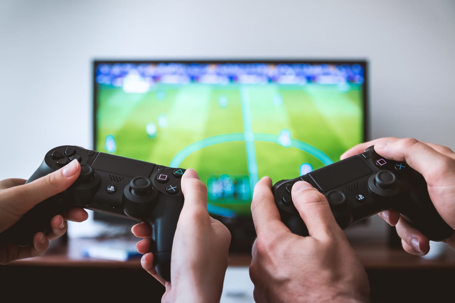 Twee mensen met twee PlayStation-controllers in hun handen voor een tv met een multiplayer-voetbalgame die ze samen spelen.