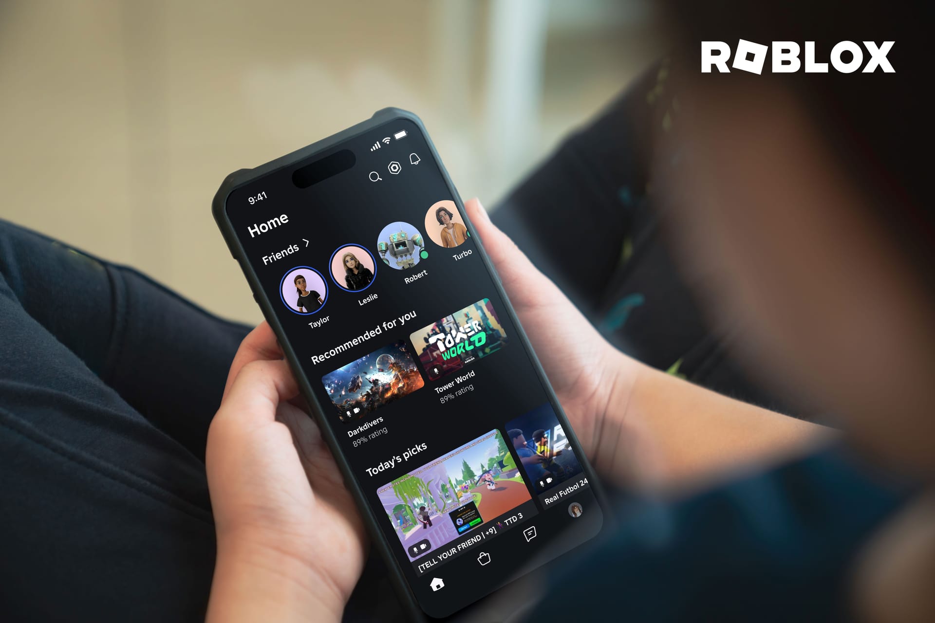 A person holding a phone with Roblox home page displayed on the screen.
