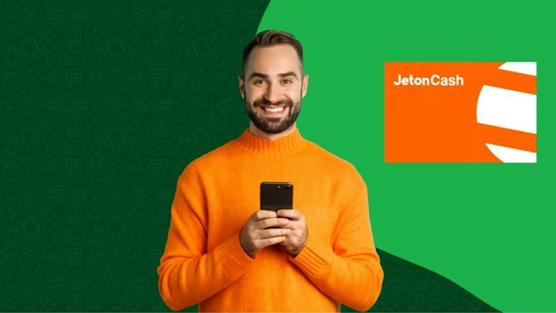 Een man in een oranje trui houdt zijn mobiele telefoon met het Jeton Cash logo naast zich.