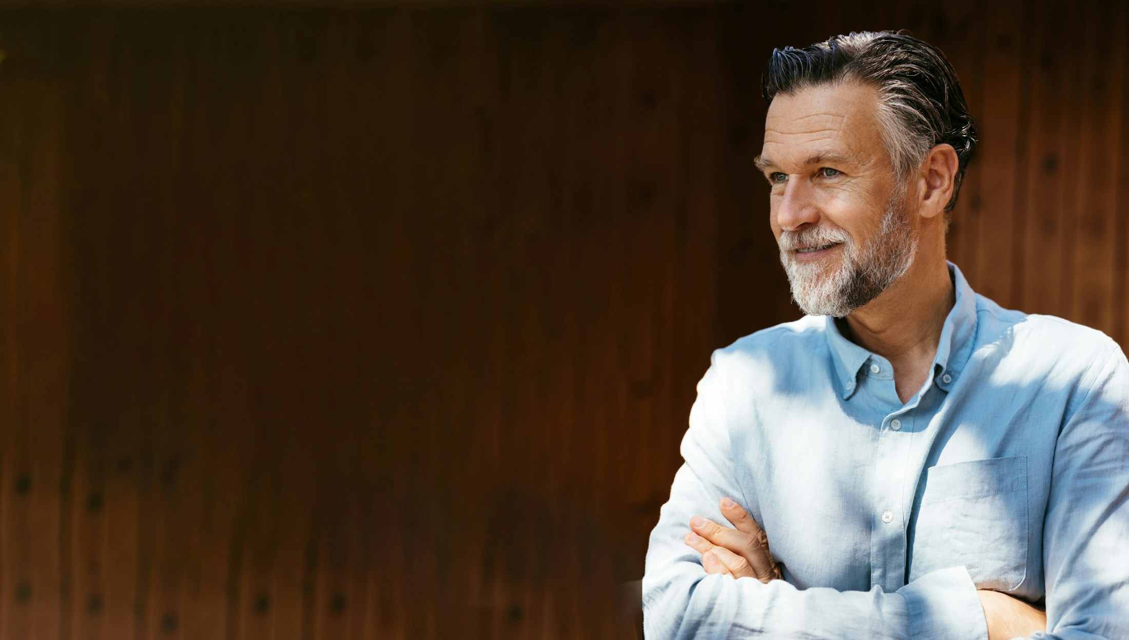 smiling man with folded arms in front of wood textured back drop