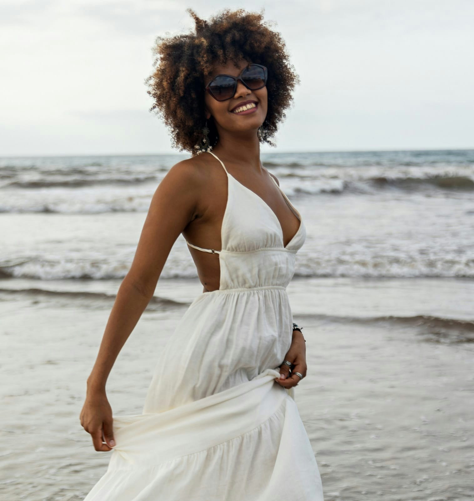 smiling woman with sunglasses wearing white dress on beach