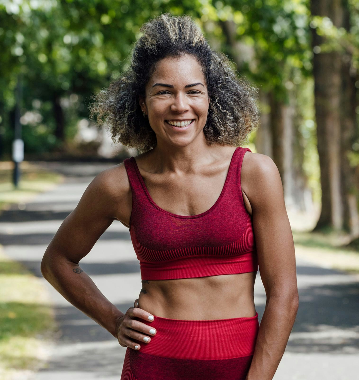 smiling woman curly hair in red athletic wear at a park