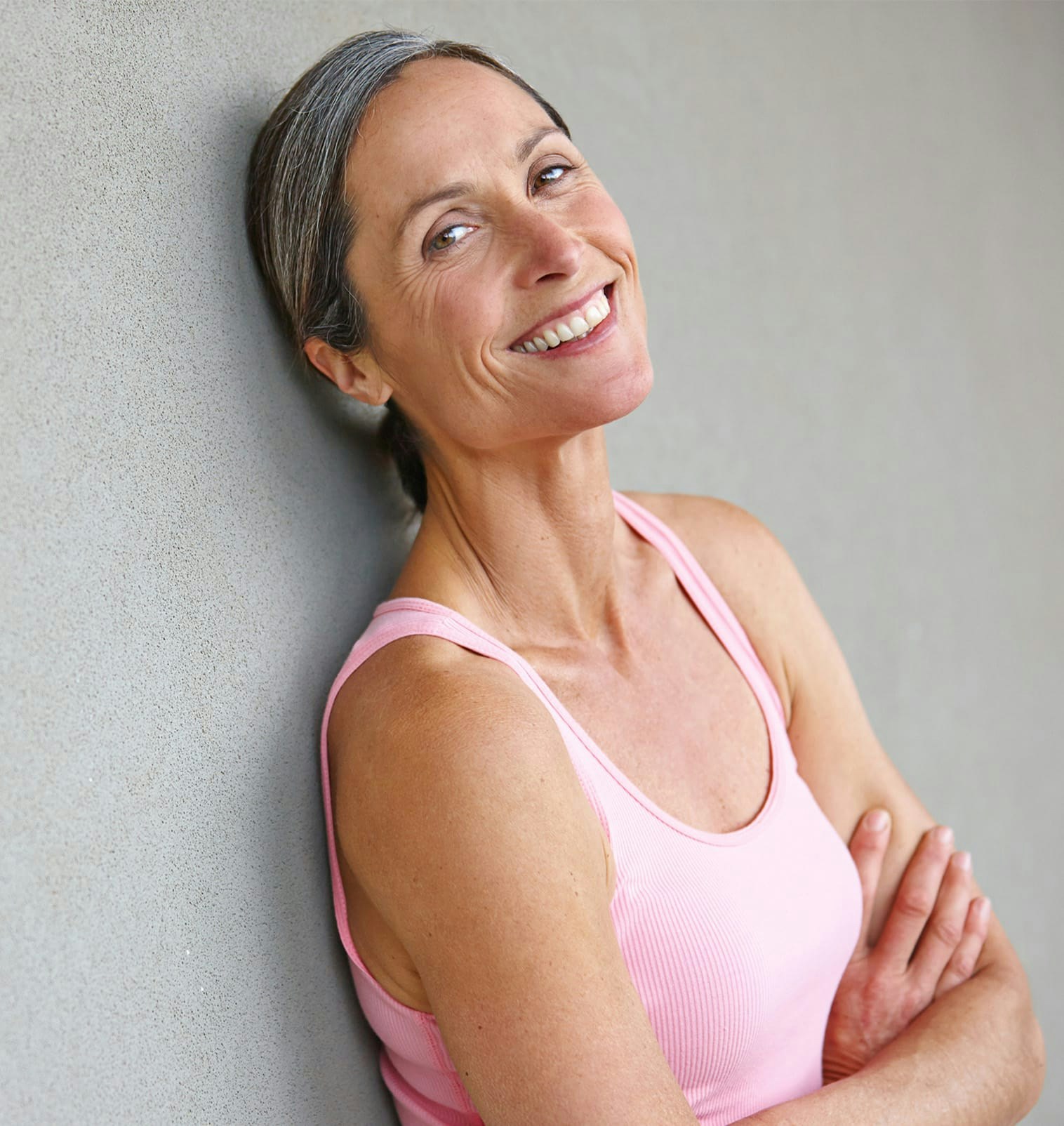 smiling woman in pink athletic wear leaning against wall with arms crossed