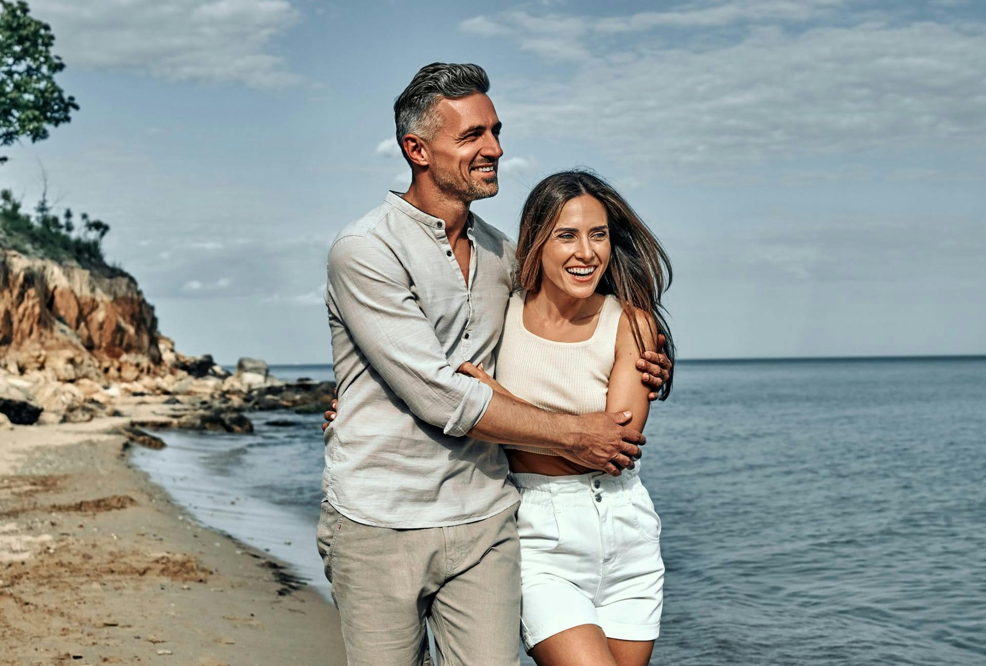 smiling couple holding each other while walking on beach
