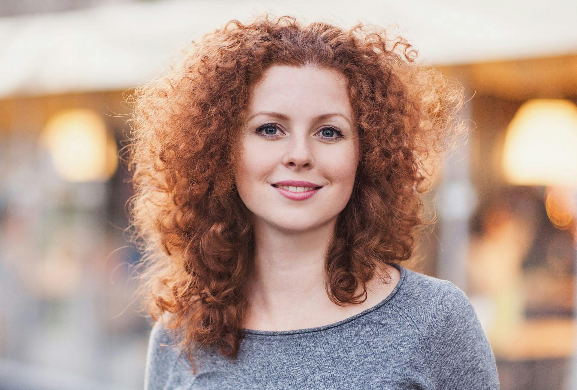 woman with curly hair wearing grey shirt smiling