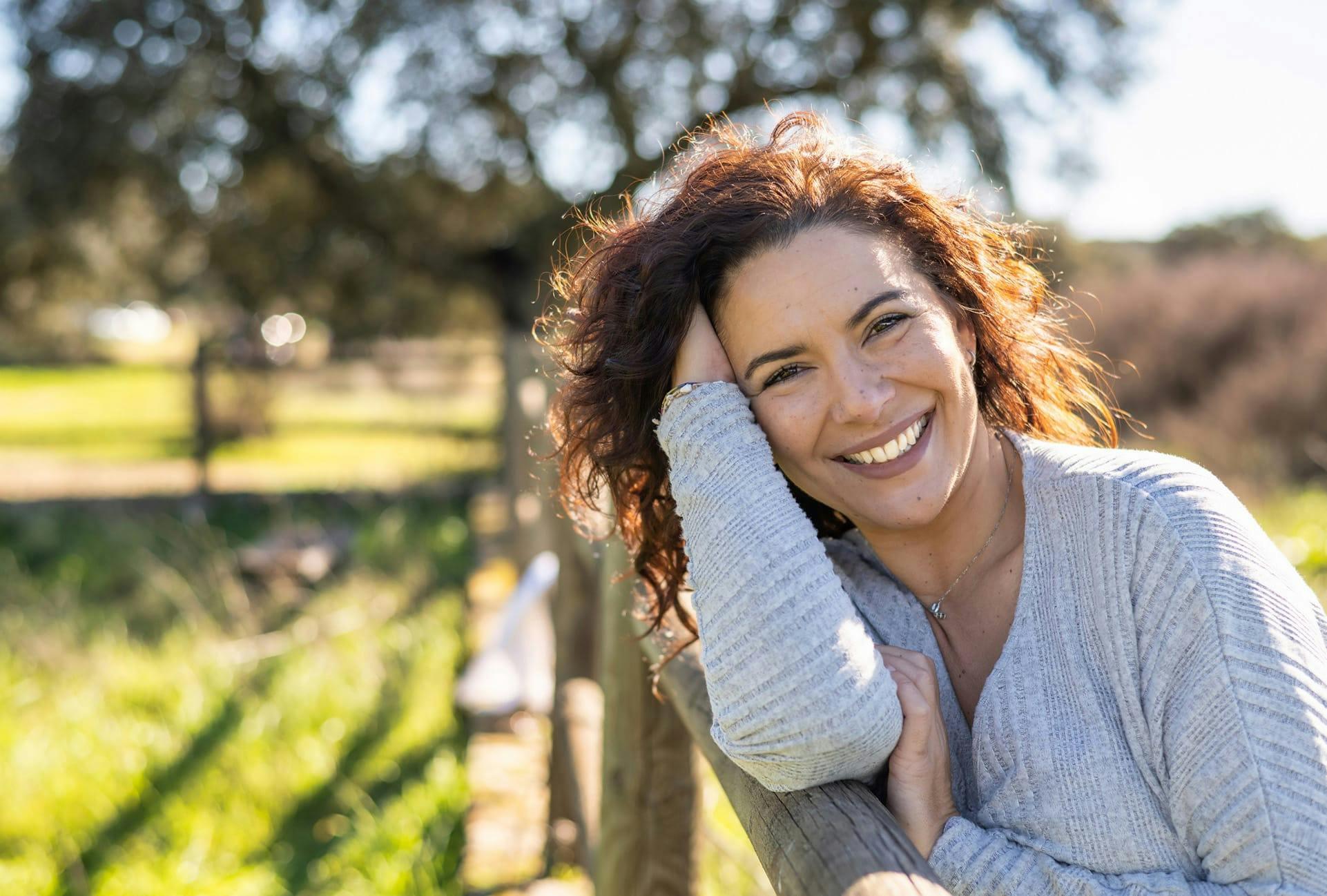 smiling woman leaning on fence holding head