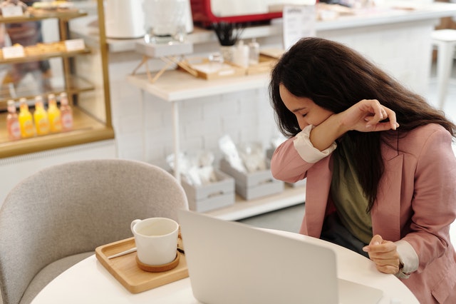 woman sneezing and sitting in front of laptop