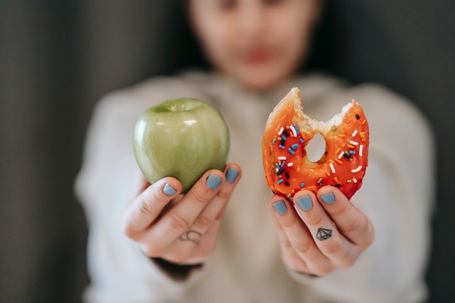 woman holding apple and half eaten donut