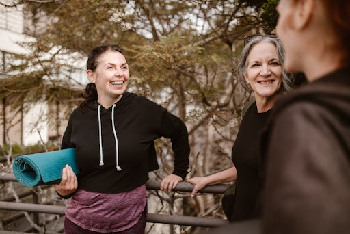 three woman talking and one is holding yoga mat