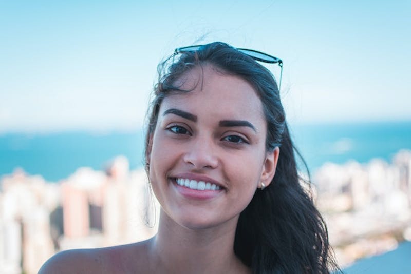 smiling woman with sunglasses on her head and a city in the background