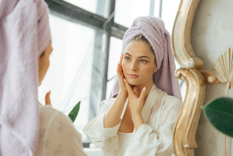 woman in a towel looking at her face in the mirror