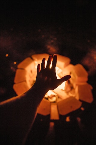 Campfire at night with a hand warming up
