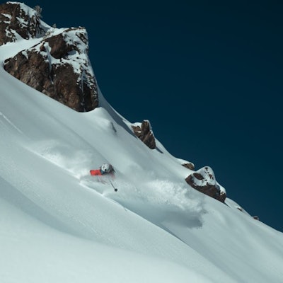 Skieur descendant une pente verticale, la poudreuse le recouvre presque, on peut apercevoir son casque blanc et un bout de sa veste rouge