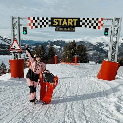 People ready to go sledding, seated under the starting arch in Courchevel Moriond.