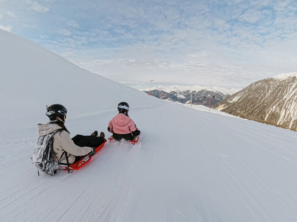 Deux personnes descendant la piste sur des luges séparées à Courchevel Moriond.