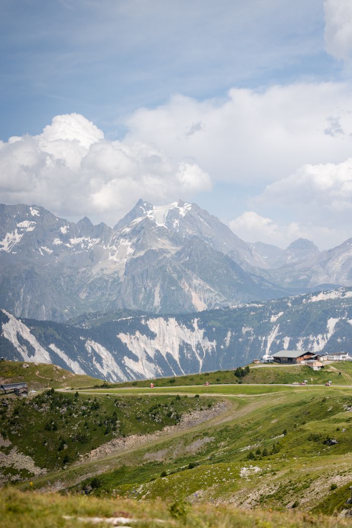 Paysage alpin avec montagnes enneigées, prairies verdoyantes et ciel nuageux.