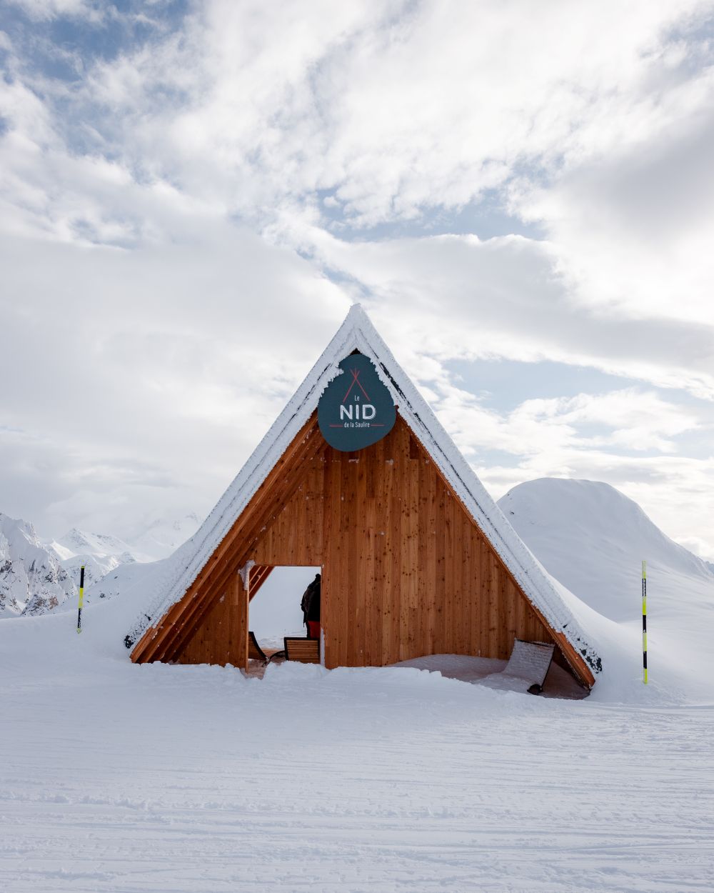 Cabane en bois au milieu d’un paysage enneigé, entourée de montagnes.